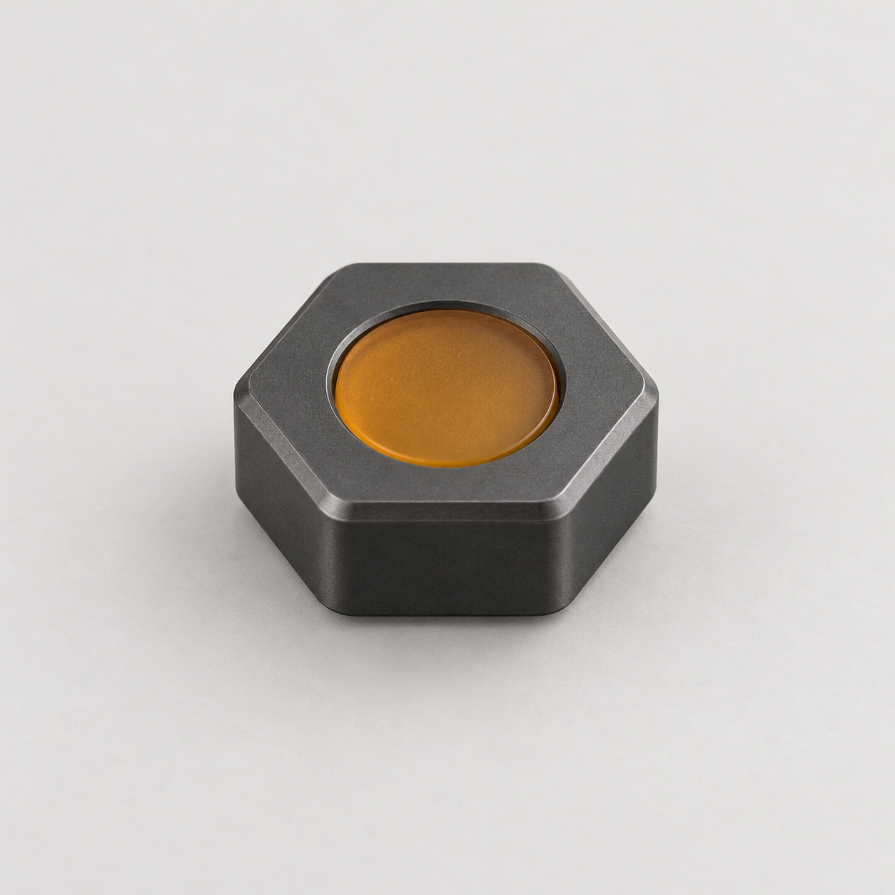 Graphite hexagonal verification token with an amber circular inset on a plain background